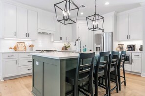 A modern kitchen with white cabinets, a central island with bar stools, and pendant lighting. - Green Retreat on Proctor - 3.5 Bathrooms (Waco)
