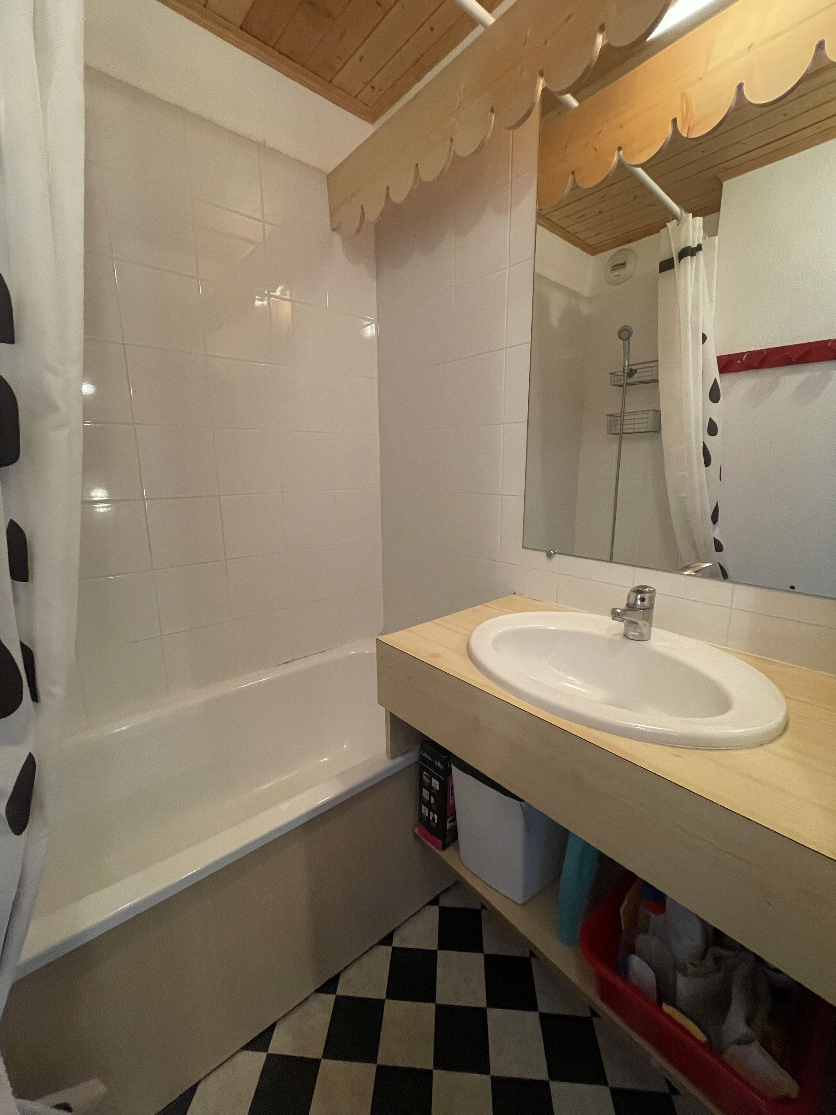 A bathroom with a white bathtub, a sink with a wooden countertop, a mirror, and a checkered floor.