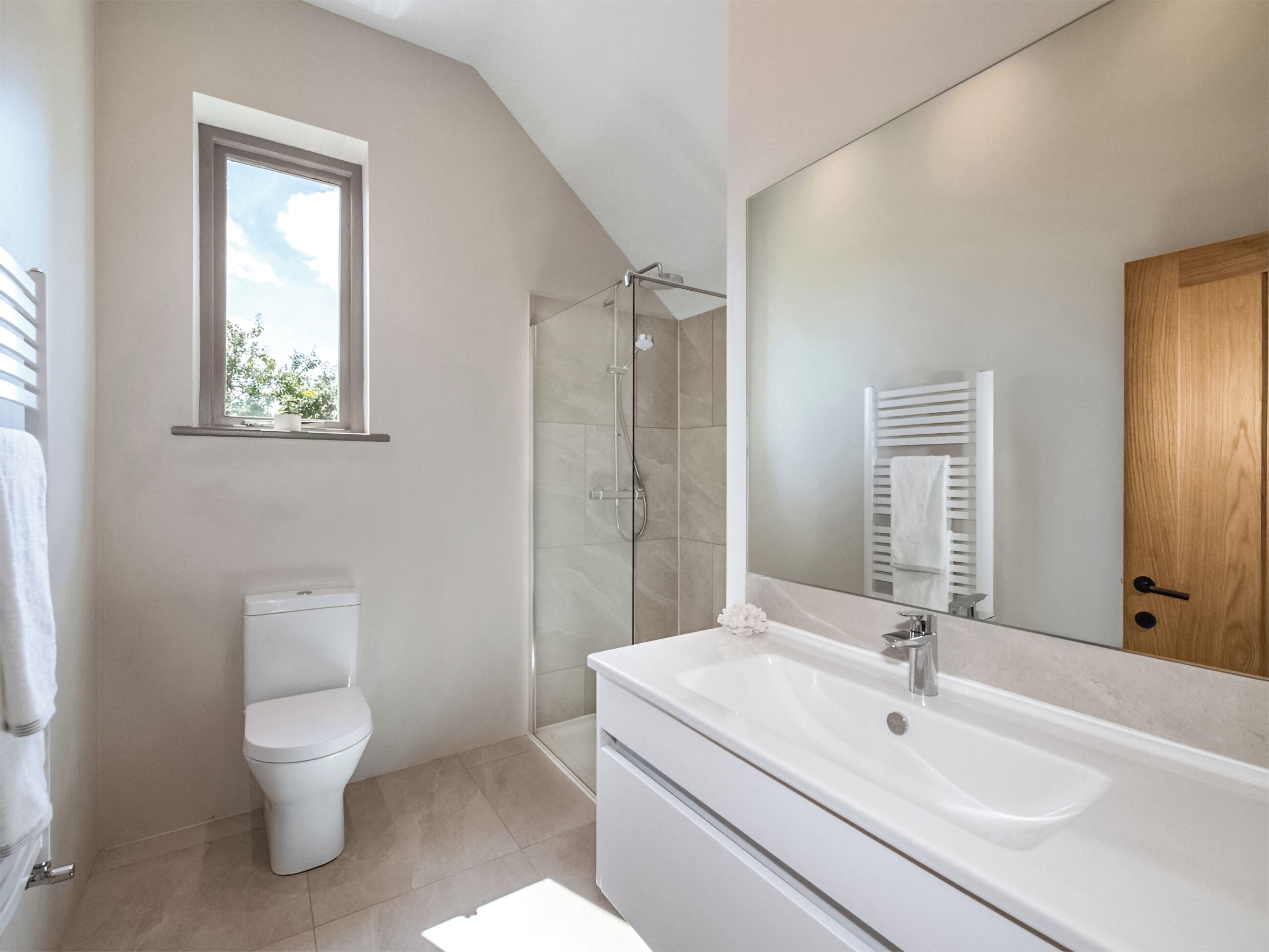 A modern bathroom with a toilet, shower, sink, and a large mirror.