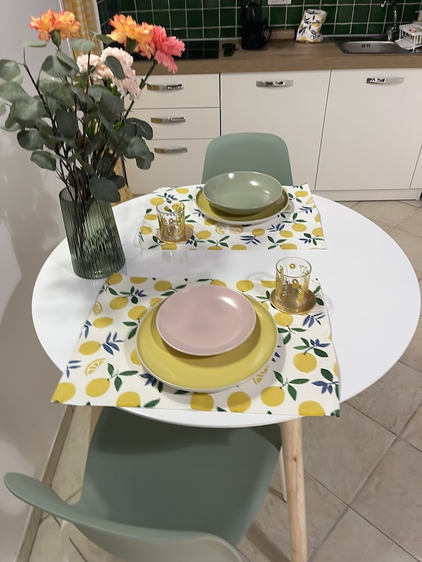 A dining table set with plates, glasses, and a vase with flowers. - Small apartment in the heart of Monti, just a stone's throw from the Colosseum (Roma)