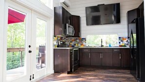 A modern kitchen with dark wood cabinets, a stainless steel microwave, and a large TV mounted above the counter.