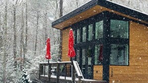 A wooden cabin with large windows, a deck, and a staircase leading to the entrance.