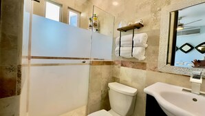 Une salle de bain avec une douche à parois de verre, des toilettes, un lavabo et un miroir doté d’un cadre décoratif.