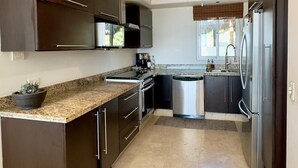 Une cuisine moderne avec des meubles de couleur sombre, un plan de travail en granit, un four encastré, un lave-vaisselle et un réfrigérateur.