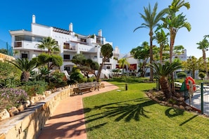 A white building with multiple balconies, surrounded by palm trees and a well-maintained lawn. - Finca San Antonio | Sunny Apartment with Large Terrace & Pool Views (Mijas Pueblo)