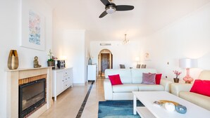 Una sala de estar moderna con chimenea, sofás blancos, una mesa de centro y un ventilador de techo.