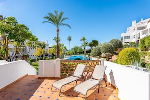 A rooftop terrace with a pool, palm trees, and lounge chairs.