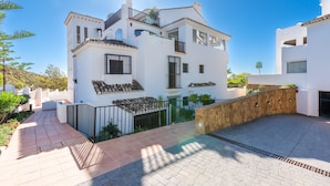 Un edificio moderno blanco con balcón, un patio empedrado y una pared de piedra.