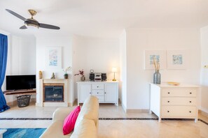 Un salon comprenant un canapé, un téléviseur, une cheminée, un ventilateur de plafond et un meuble blanc.