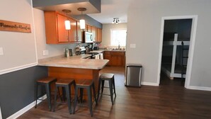 Een moderne keuken met houten kastjes, een centraal eiland met krukken en een zichtbare prullenbak.