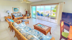 Ein großzügiges Wohnzimmer mit einer großen Couch, einem Couchtisch und einem Fernseher. Ein Balkon bietet Blick auf den Strand.