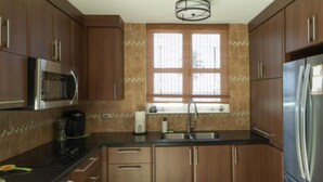 A modern kitchen with wooden cabinets, stainless steel appliances, a window with blinds, and a tiled backsplash. - Relaxing Beachfront Condo (Aguada)