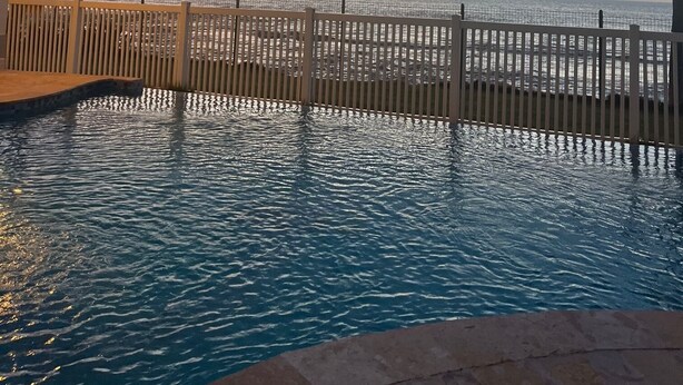 A pool with a wooden fence, palm trees, and a sunset view. - Relaxing Beachfront Condo (Aguada)