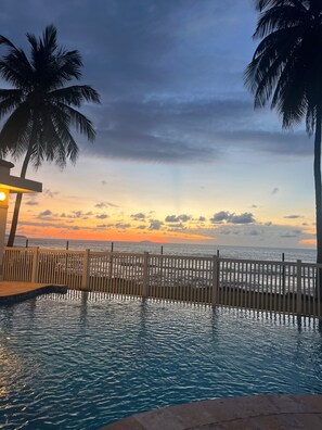 A pool with a wooden fence, palm trees, and a sunset view. - Relaxing Beachfront Condo (Aguada)