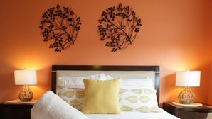 A hotel room with a bed, two nightstands, a lamp on each nightstand, a yellow and white patterned bedspread, a white towel, a yellow pillow, and two wall decorations. - Relaxing Beachfront Condo (Aguada)