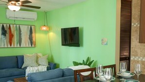 A living room with a blue sofa, a dining table set with plates and glasses, and a ceiling fan. - Relaxing Beachfront Condo (Aguada)