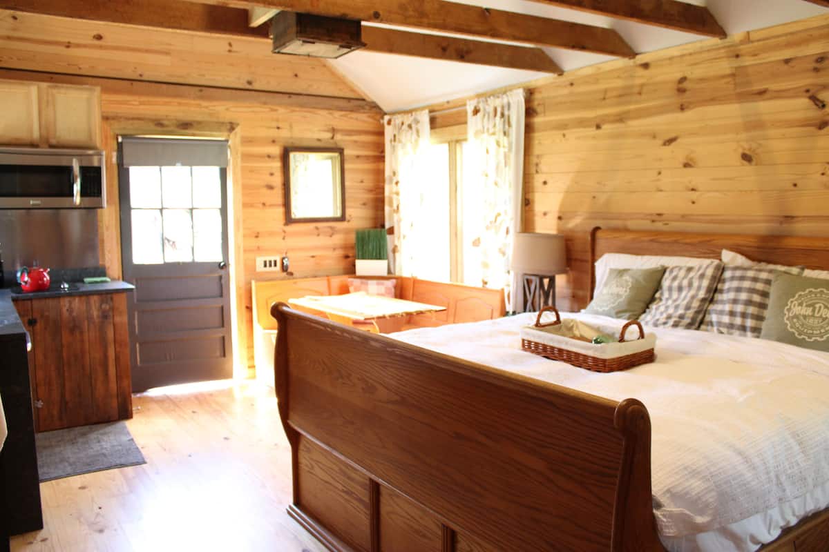A wooden cabin-style bedroom with a bed, bedside table, lamp, and a window with curtains.