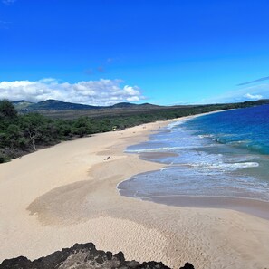 A beach with clear blue water, sandy shore, and distant hills.