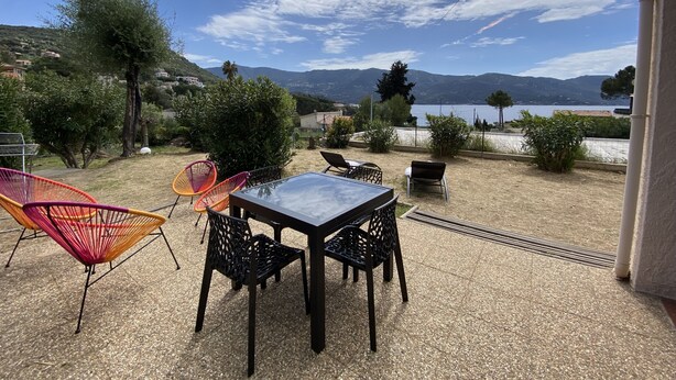 An outdoor patio with a table and chairs, a view of a lake, and surrounding greenery. - Appartement les Marines, Accès Plage à Pied. Vue Mer. Grande Terrasse (Casaglione)