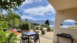 An outdoor patio with a table and chairs, a view of the sea and mountains, and a covered area with a table and chairs. - Appartement les Marines, Accès Plage à Pied. Vue Mer. Grande Terrasse (Casaglione)