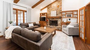 Una sala de estar con chimenea de piedra, vigas de madera, un sofá, una mesa de centro y una mesita auxiliar.
