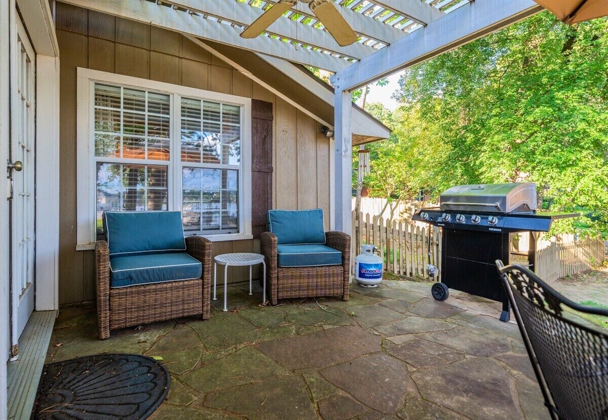 Un patio couvert avec des meubles en osier, un barbecue et une bouteille de propane.