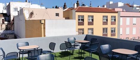 Een buitenzitplaats met tafels en stoelen op kunstgras, omringd door gebouwen met uiteenlopende architectuur.