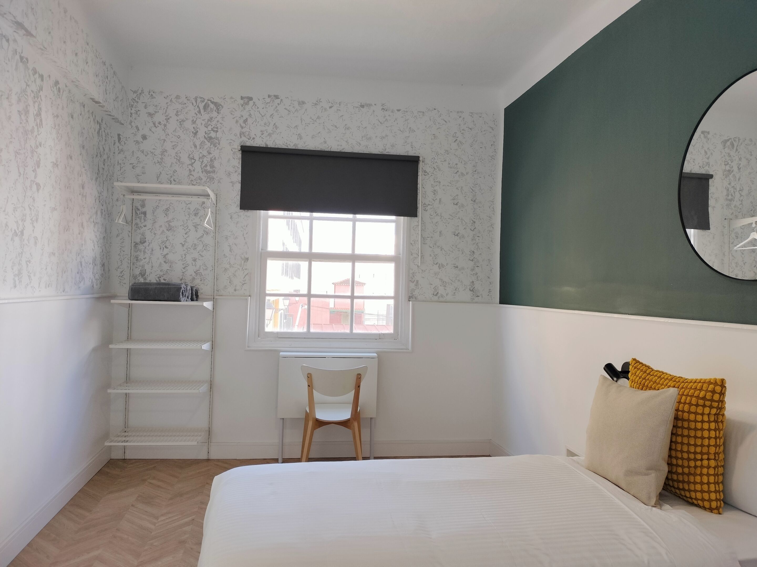 A bedroom with a bed, a desk, a chair, a window, and a mirror.