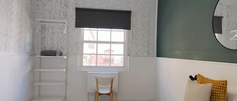 A bedroom with a bed, a desk, a chair, a window, and a mirror.