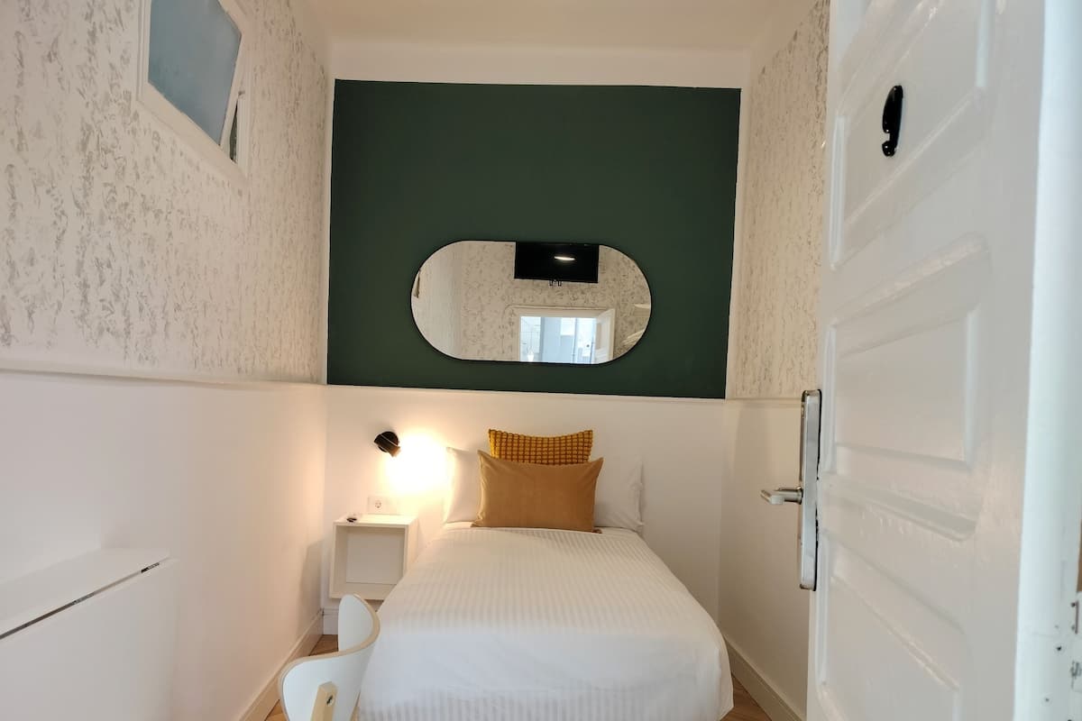 Un dormitorio pequeño y acogedor con cama, mesita de noche con lámpara, espejo y puerta.