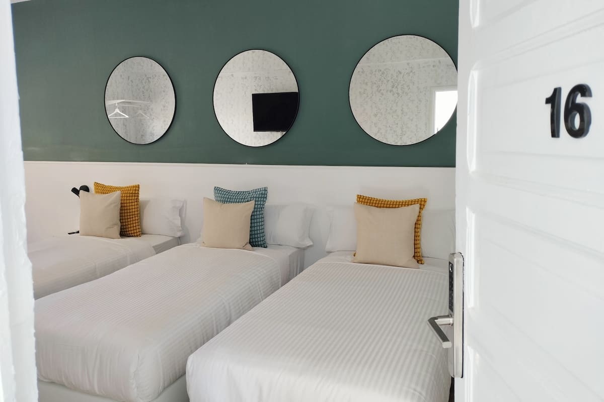 Habitación de hotel con dos camas, una pared verde y tres espejos redondos.