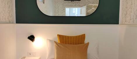 A hotel room with a bed, a nightstand, a wall-mounted TV, and a mirror reflecting the room.