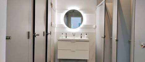 A modern bathroom with a central sink, a round mirror, and a light fixture above it.