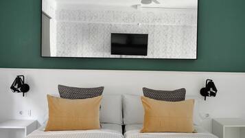 Cama doble con ropa de cama a rayas, dos almohadas, un televisor montado en la pared y dos apliques.