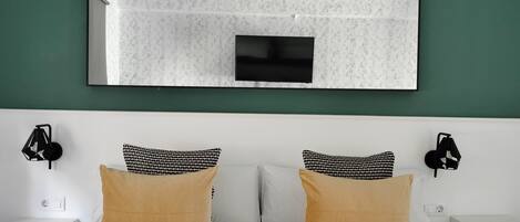 Cama doble con ropa de cama a rayas, dos almohadas, un televisor montado en la pared y dos apliques.