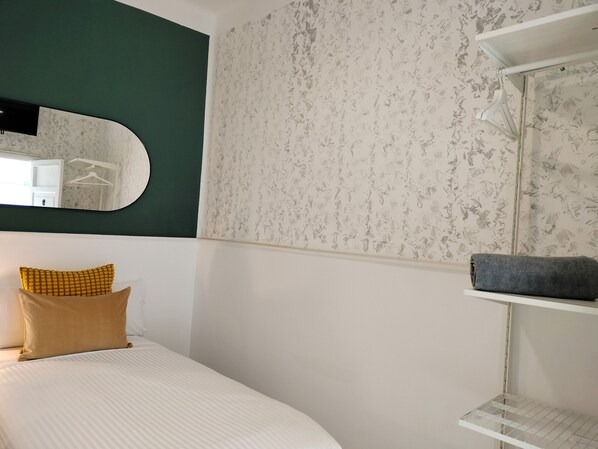 A bedroom with a bed, a mirror, a wall with a floral pattern, a shelf with a towel, and a hanging light fixture. - Room27 (San Cristóbal de La Laguna)