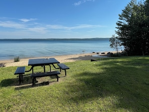 Enjoy a serene lakeside picnic with a table and benches on a grassy area overlooking the lake.