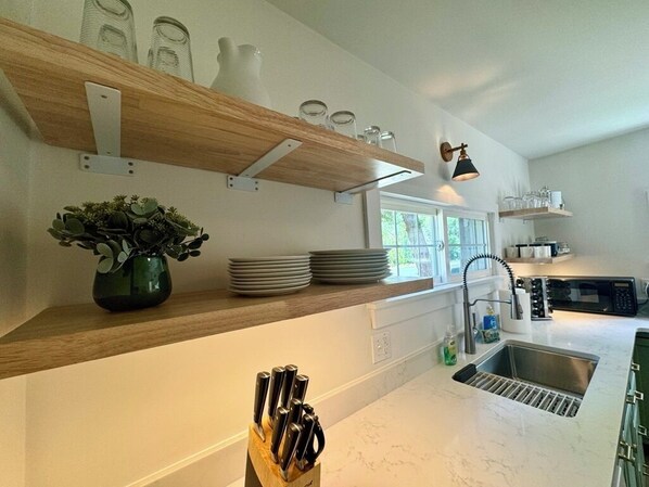 A modern kitchen with a wooden shelf, a vase with green plants, a knife block, and a sink.