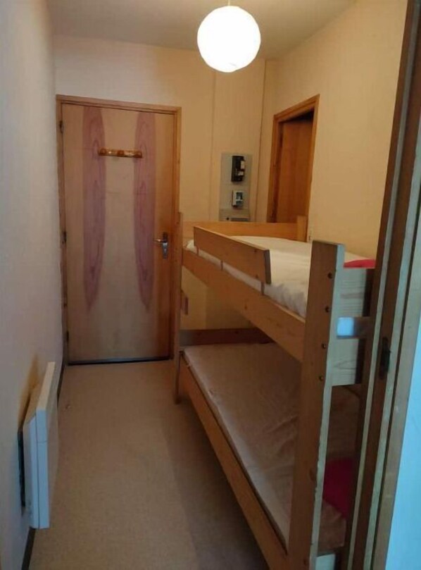 A narrow room with a bunk bed, a wooden door, and a small bedside table.
