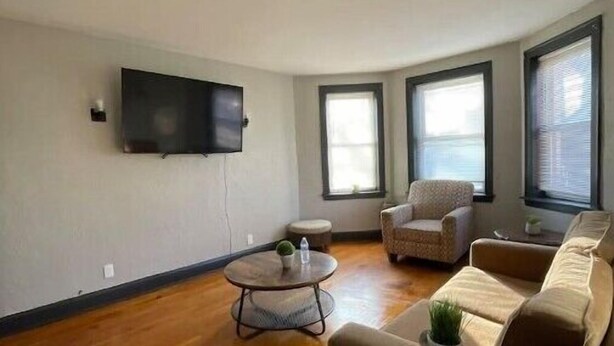 A living room with a sofa, armchairs, a coffee table, and a flat-screen TV mounted on the wall.