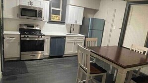 A compact kitchen with white cabinets, a microwave, stove, and a ceiling fan.