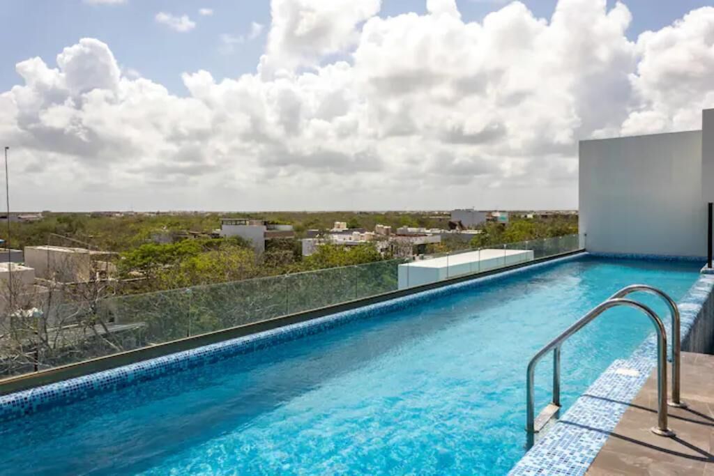 A rooftop swimming pool with clear blue water, surrounded by a glass barrier and metal railings.