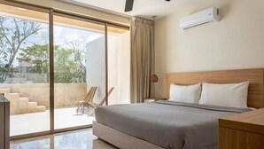 Une chambre à coucher moderne avec un grand lit, une tête de lit en bois, une table de chevet et une chaise près d’une porte-fenêtre coulissante donnant sur un balcon.