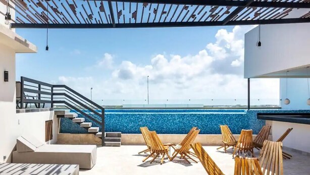 Une terrasse sur le toit avec une piscine, des chaises en bois et un escalier menant à un niveau supérieur.