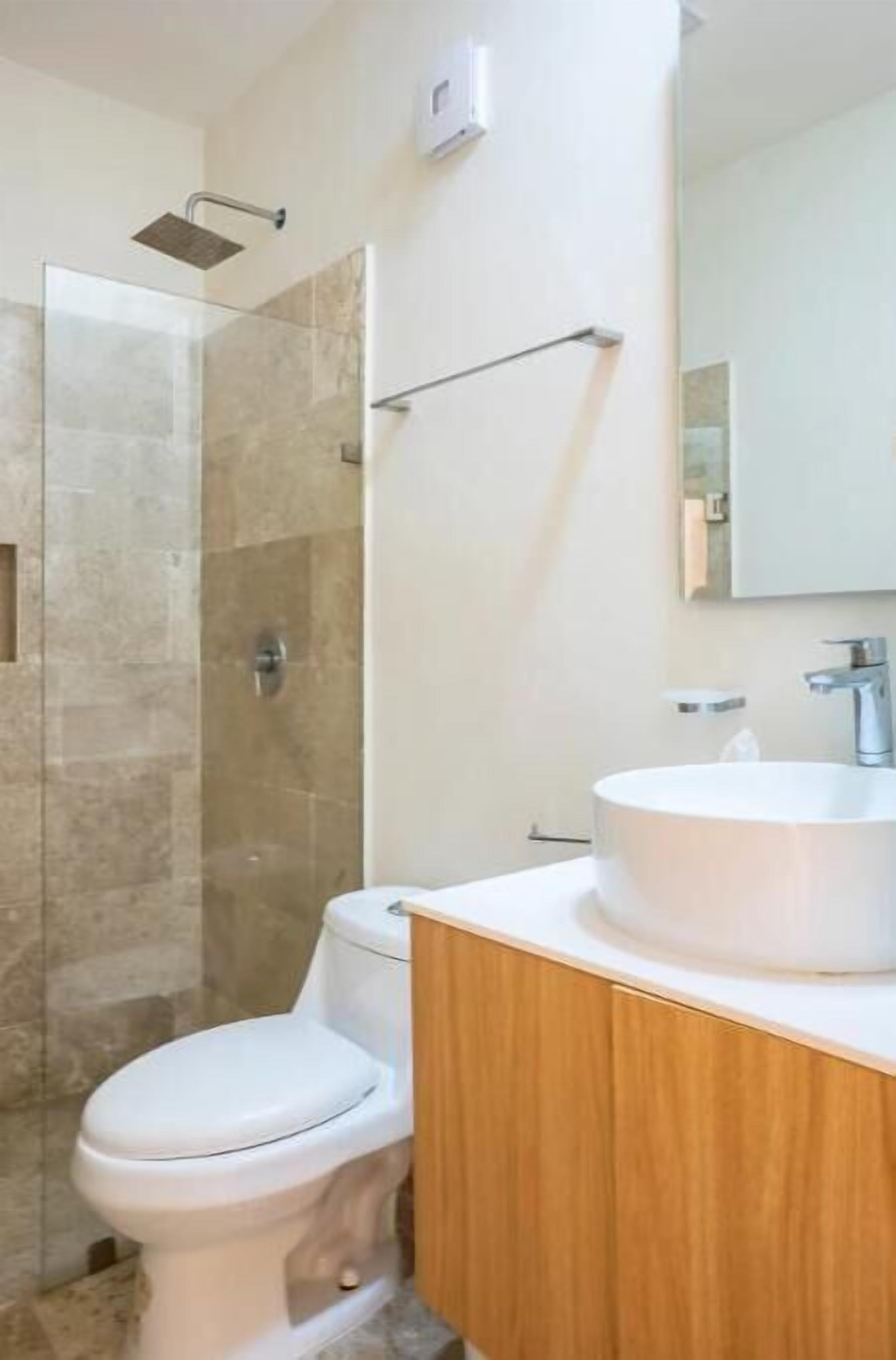 A modern bathroom with a glass-enclosed shower, a white toilet, and a wooden vanity with a round sink.