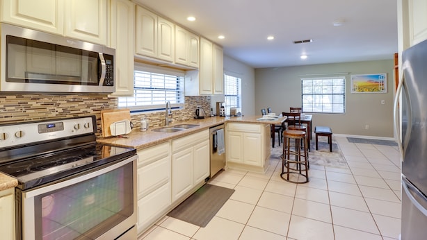 A modern kitchen with white cabinets, stainless steel appliances, and a dining area with a bar stool. - Lake Days & Golf Outings: Summerfield Group Escape (Summerfield)