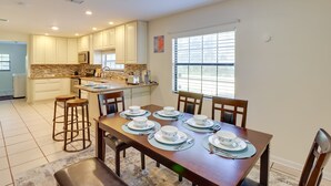 A modern kitchen with white cabinets, a stone backsplash, and a dining area set for six with white plates and blue napkins. - Lake Days & Golf Outings: Summerfield Group Escape (Summerfield)