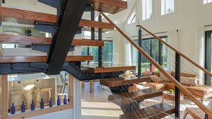 A modern interior with a multi-level wooden staircase, glass railings, and a view of the outdoors. - SOL® Catskills Mnt view, Sauna, Hot Tub, Fire Pit, Min to Plattekill & Belleayre (New Kingston)