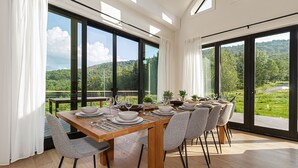 A dining area with a table set for four, large windows, and a view of a green landscape. - SOL® Catskills Mnt view, Sauna, Hot Tub, Fire Pit, Min to Plattekill & Belleayre (New Kingston)