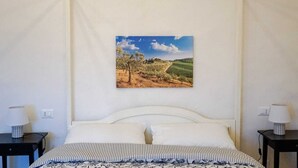 Ein Schlafzimmer mit einem Bett, zwei Nachttischen, einem Wandbild mit einer Landschaft und einer weißen Decke.